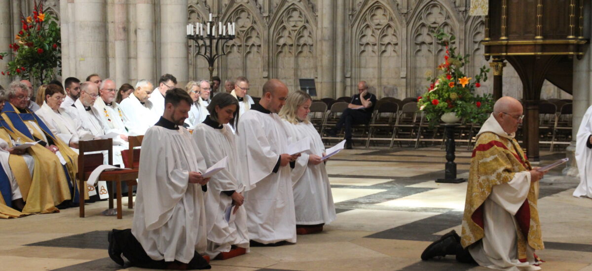 deacon ordination service in york minster. four deacons and the archbishop of york, all kneeling.
