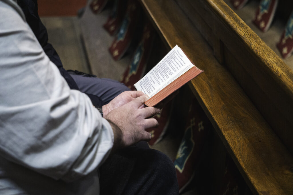 Two men reading a Bible together seated in a church pew.