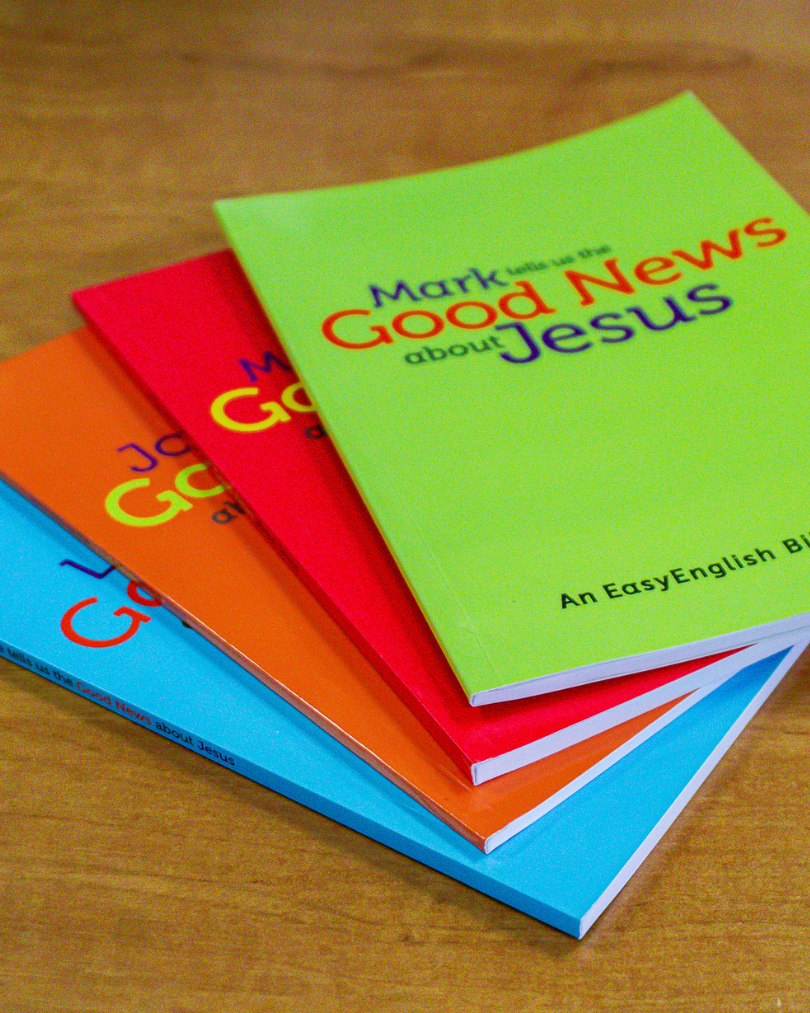MissionAssist's EasyEnglish Gospels in bright colours fanned on a table.